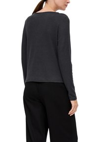 Langärmliges graues Oberteil aus weichem Stoff, mit rundem Halsausschnitt und lockerer Passform, kombiniert mit schwarzen Hosen.