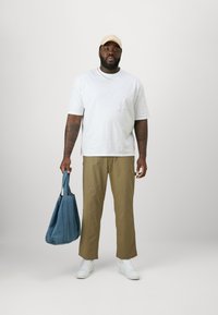 Lässiges Outfit mit einem weißen T-Shirt mit kurzen Ärmeln, khakifarbenen Hosen und weißen Sneakers. Hält eine blaue Denim-Tasche.