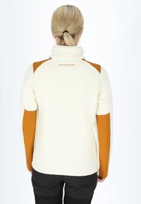 White fleece jacket with orange shoulder and sleeve accents. Features a high collar and "SWEDEMOUNT" logo on the back. Textured fabric.