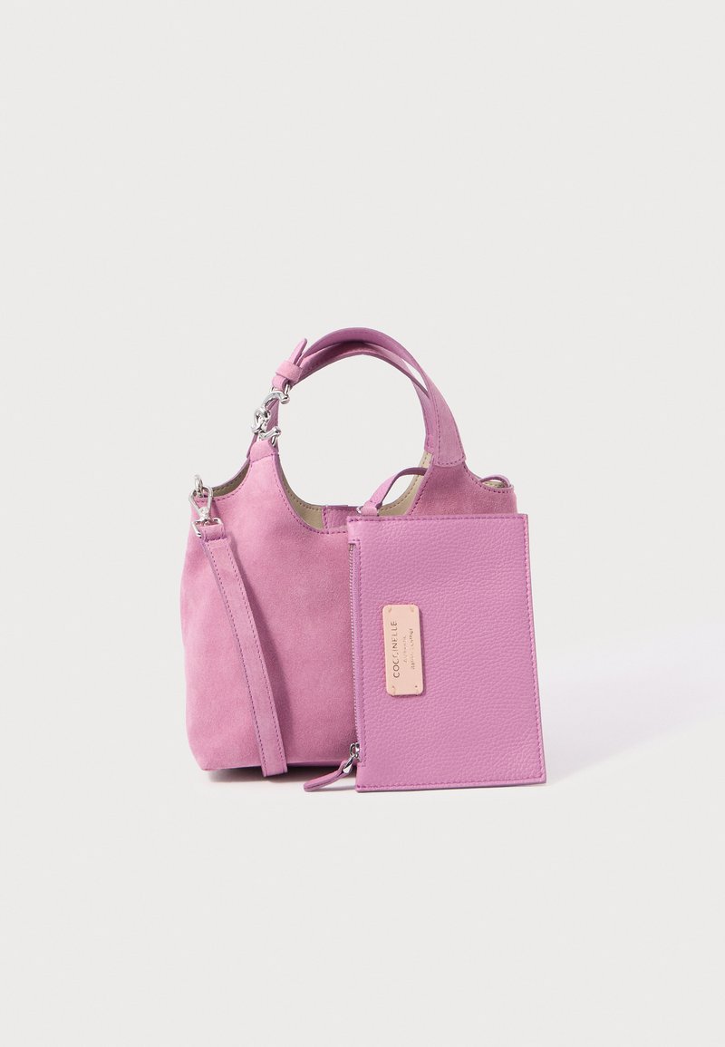 Μικρή ροζ σουέντ τσάντα χειρός με διπλούς λαβές και αποσπώμενο ιμάντα, συνοδευόμενη από αντίστοιχη ροζ υφασμάτινη θήκη με φερμουάρ και ετικέτα της μάρκας.