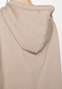 Primo piano di un tessuto di felpa beige che mostra il retro e il cappuccio attaccato con cuciture visibili e una texture morbida.