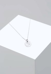 Ezüst nyaklánc texturált, kör alakú medállal, kis csatlakozó hurokkal és finom lánccal. Egyszerű és elegáns kialakítás.