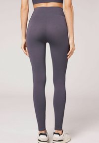 Rippens, hochgeschnittene Leggings in Dunkelgrau mit figurbetontem Schnitt und glatter Textur, kombiniert mit weißen und schwarzen Sportschuhen.