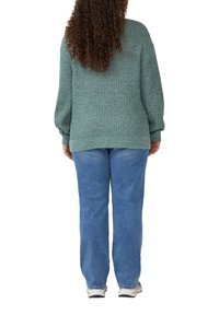 Grüner gestrickter Pullover mit gerippter Struktur, Ballonärmeln und lockerer Passform, kombiniert mit hellblauen gerade geschnittenen Jeans und weißen Sneakers.