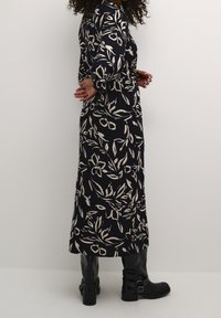 Pitkä, laivastonsininen mekko, jossa on kukkakuvio kermanvärisenä. Mekossa on pitkät hihat ja löysä istuvuus, yhdistetty mustiin polven korkeisiin saappaisiin.