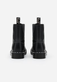 Botas de tobillo de cuero negro con un diseño cosido, punta redonda y suela de goma gruesa. Cuenta con tiradores negros con letras blancas en la parte posterior.