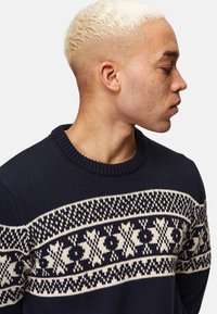 Navy knitted sweater with a round neckline, featuring a contrasting cream snowflake pattern across the chest and shoulders.