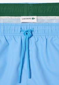 Niebieskie kąpielówki z elastycznym pasem, regulowanym sznurkiem i zieloną górną częścią. Posiadają białą siateczkową podszewkę oraz metkę z logo.