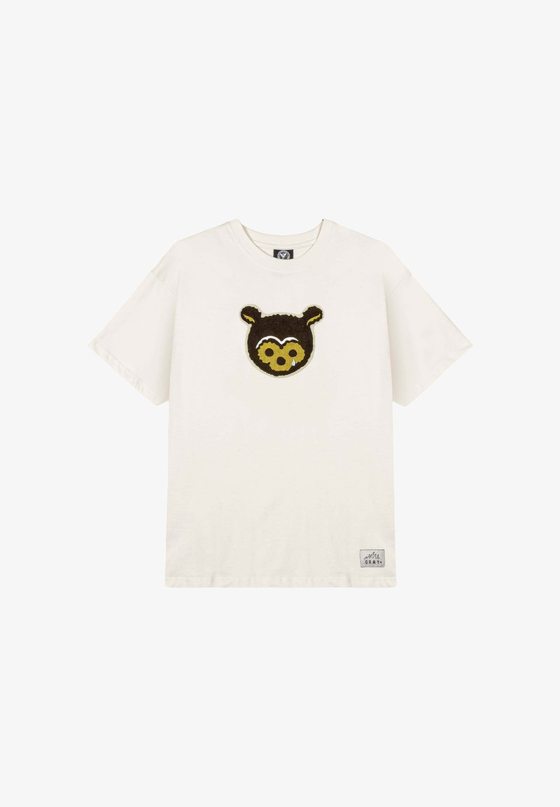 Bawełniana koszulka w kolorze kremowym z nadrukiem twarzy brązowego misia z przodu. Krótkie rękawy, okrągły dekolt i mała metka marki u dołu po lewej stronie.