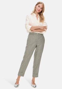 Helle beige Bluse mit Kragen, kombiniert mit grauen karierten Hosen mit umgeschlagenem Saum und einem grünen Knopfdetail. Silberne Ballerinas.