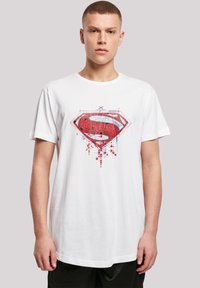 White cotton t-shirt featuring a red Superman logo graphic with pixelated details. Short sleeves and a round neckline.