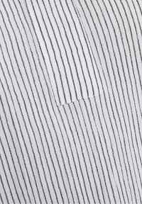 Tissu blanc avec de fines rayures verticales noires et une petite poche rectangulaire cousue au centre.