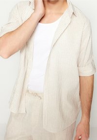 Lyhythihainen raidallinen paita beigen värisenä, jossa vaaleanruskeat raidat, valmistettu kevyestä kankaasta. Edessä napillinen ja pehmeä kaulus.