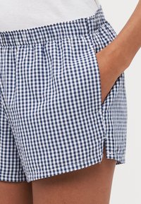 Marineblauwe en witte geruite shorts met een elastische tailleband, zijzakken en een splitzoom voor extra bewegingsvrijheid. Gemaakt van lichte stof.