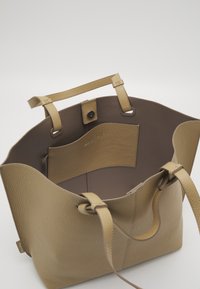 Torebka tote w kolorze jasnobrązowym, z podwójnymi uchwytami, z zapięciem na magnes oraz wewnętrzną kieszenią na jednolitym białym tle.