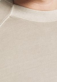 Beżowa bluzka z długim rękawem o ryflowanej teksturze i okrągłym dekolcie. Posiada gładką, miękką tkaninę oraz wszyte akcenty wzdłuż szwów.
