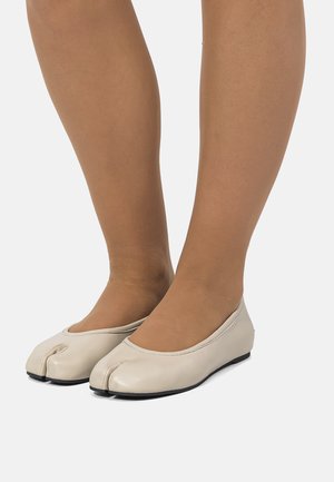 Zapatos planos beige con un diseño único de punta partida, material de cuero suave y suela flexible de goma negra.