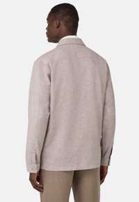 Camisa de textura marrón clara con mangas largas, detalles de botones en los puños y un cuello clásico. Presenta un corte relajado y un patrón sutil.