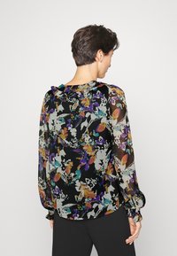 Blusa floral em tecido preto transparente, apresentando padrões multicoloridos em roxo, laranja e teal. Decote com babados e punhos elásticos.