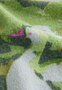 Kuvioitua kangasta, jossa on maastokuvio vihreillä, valkoisilla ja vaaleanpunaisilla sävyillä; pehmeä, pörröinen pinta; lähikuva korostaa yksityiskohtia.