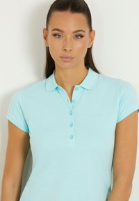 Hele sinine polo särk, mis on valmistatud pehmest kangast, omab kaelusega kaela ja nööpide rida. Lühikesed varrukad ja peen broderaaditud logo detail.