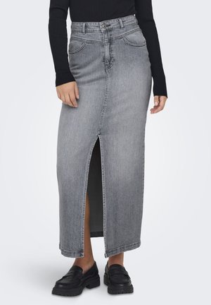 Frau trägt einen grauen Denim-Midi-Rock mit hoher Taille und einem seitlichen Schlitz, kombiniert mit einem schwarzen Langarmshirt und schwarzen Loafers.