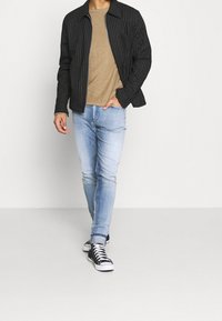 Musta raidallinen takki, jossa on kaulus, beigenvärinen t-paita, vaaleansiniset farkut ja mustat korkeakorkoiset lenkkarit, joissa on valkoiset nauhat.