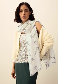 Gaiši zils šalle ar kokteiļu motīviem, kas uzlikta uz krēmkrāsas kardigāna un sekvīšu topa; zaļa svārku kārta; teksturētas rakstainas un slāņainas auduma kombinācijas.