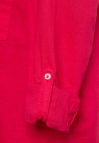 Fuchsia Leinenhemdärmel mit einem einzelnen weißen Knopf. Der Stoff hat eine glatte Textur, und das Design der hochrollbaren Manschette weist eine subtile Falte auf.