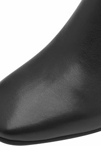 Botín de cuero negro hasta el tobillo con punta afilada y textura suave. El diseño presenta una silueta elegante y un perfil minimalista.