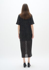 Svart lång klänning med korta ärmar, genomskinligt material, strukturerat mönster, midikalvlängd, bärs med svarta klackskor med blockhäll.