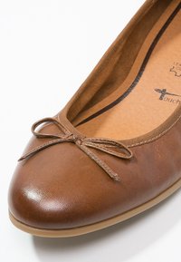 Ballerine en cuir marron avec un petit nœud décoratif sur l\'avant arrondi et une semelle intérieure rembourrée visible à l\'intérieur de la chaussure.