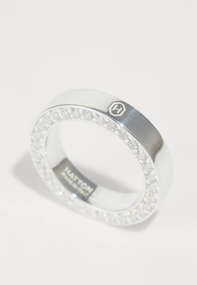 Anillo de plata con una banda blanca suave, adornado con una fila de cristales claros a lo largo del borde. Presenta un pequeño logotipo hexagonal.
