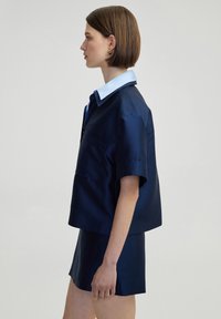 Navy satin short-sleeve shirt with a light blue collar and a chest pocket, paired with a matching navy skirt, displayed in profile.