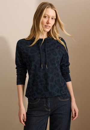 Sweatshirt bleu marine avec un imprimé léopard subtil, doté d'une capuche et de cordons de serrage, associé à un jean en denim foncé. Texture douce, coupe décontractée.