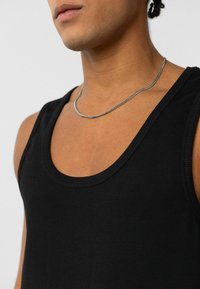 Zwarte geribbelde tanktop met een brede ronde halslijn, voorzien van een soepele textuur. Een zilveren kettinkje hangt om de nek.