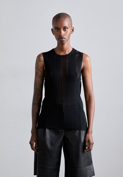 Haut sans manches noir avec des nervures verticales, fabriqué dans un matériau transparent. Porté avec un short en cuir noir taille haute.
