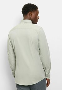 Hellgrünes Langarmhemd mit glatter Textur, Standardkragen und knöpfbaren Manschetten, mit abgerundetem Saum und dezenten Nahtdetails.