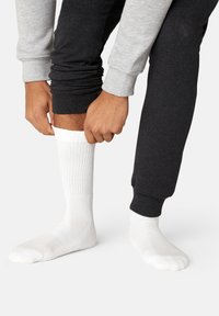 White ribbed socks being pulled up, paired with dark gray joggers featuring a cuffed hem and light gray top. Soft fabric texture visible.