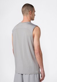 Uomo che indossa una maglietta atletica senza maniche grigia chiara e pantaloni abbinati, visto di spalle su uno sfondo bianco semplice.