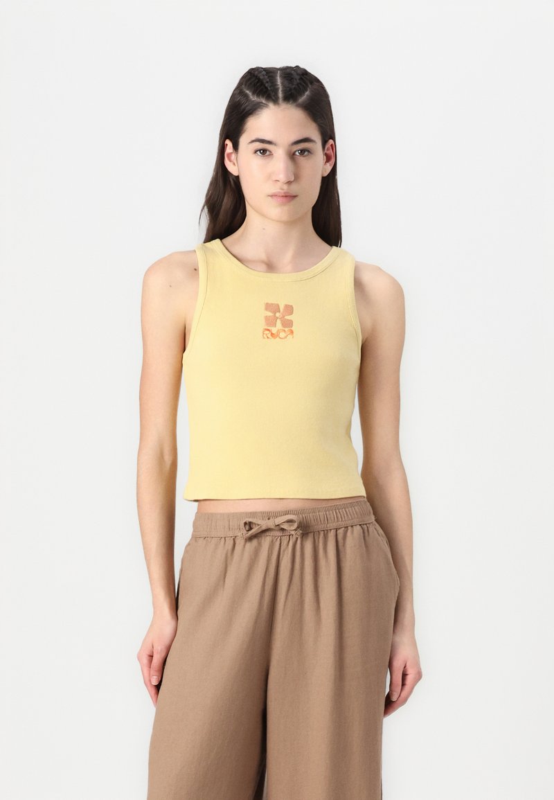 Yellow ribbed tank top with a round neckline and a small orange logo printed at the center, paired with loose brown trousers.