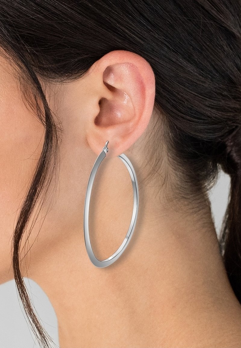 Sølv hoop ørering med en tynd, forlænget oval form, der har en glat, reflekterende overflade og en sikker låsemekanisme.