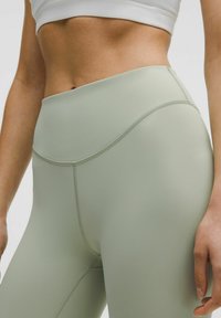 Leggings sportivi a vita alta di colore verde chiaro, realizzati in un tessuto liscio e elastico, con cuciture piatte e un design curvo discreto in vita.