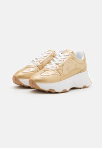 Sneakers dorati con una parte superiore lucida e testurizzata, lacci bianchi e suole bianche voluminose. Presentano sottili motivi impressi. Suola in gomma per una migliore aderenza.