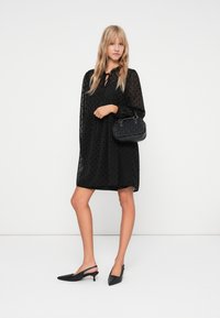 Črna obleka s pikami, ohlapnega kroja, s ključavnico na vratu in dolgimi rokavi; združena z teksturirano črno torbico in črnimi pointed slingback petami.