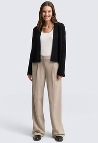 Black knitted cardigan with open front, paired with a white tank top and beige high-waisted pants. Smooth texture, relaxed fit, and wide legs.