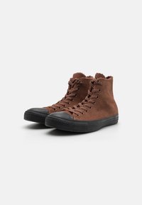 Pantofi înalți din suede maro cu capac și talpă din cauciuc negru, având eyelets din metal și detalii cusute în jurul gulerului.