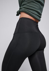 Zwarte high-waisted legging gemaakt van rekbare stof, met platte naden en een gladde textuur voor comfort en bewegingsgemak.