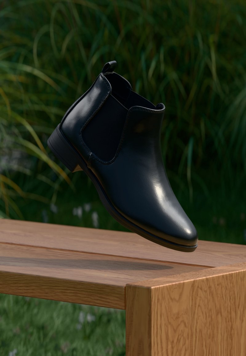 Botte Chelsea en cuir noir avec panneaux latéraux élastiques flottant au-dessus d'un banc en bois en plein air, avec un fond d'herbe verte.