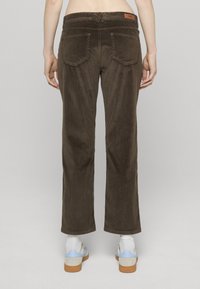 Brune kordfløyelsbukser med rette ben, baklommer, sydd detaljering og en lærmerke på linningen. Brukt med joggesko.